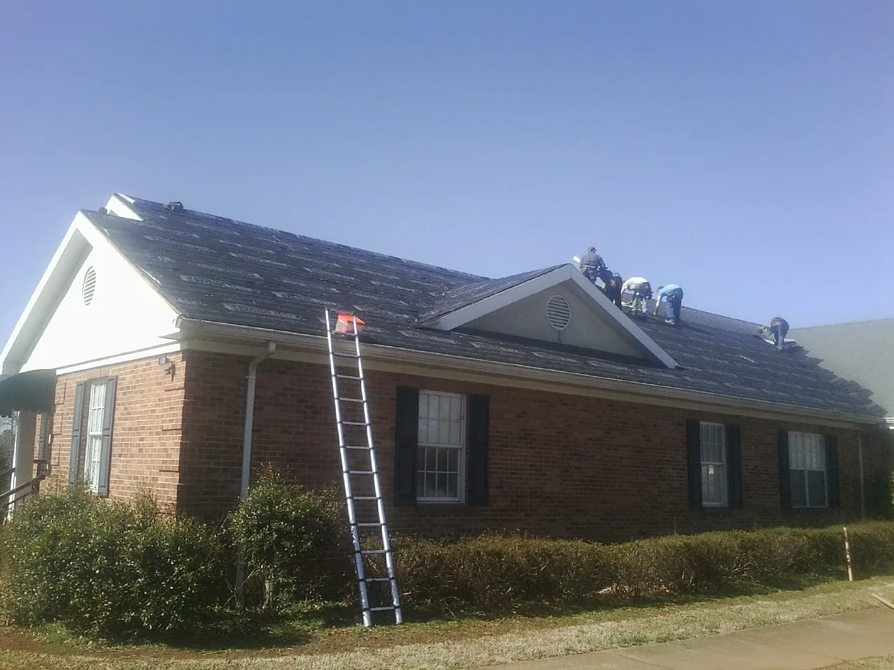 Crew tearing shingles off a brick ranch roof with a ladder set — Metal Roof Repair work by our crew in Pickens