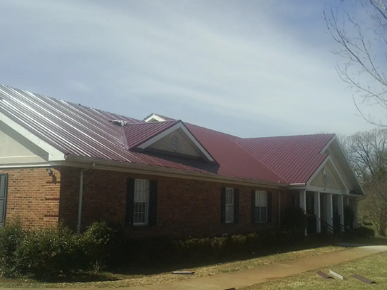 Red metal roof with gabled entries on a long brick building, from a Hail Damage Roof Repair job in Pickens